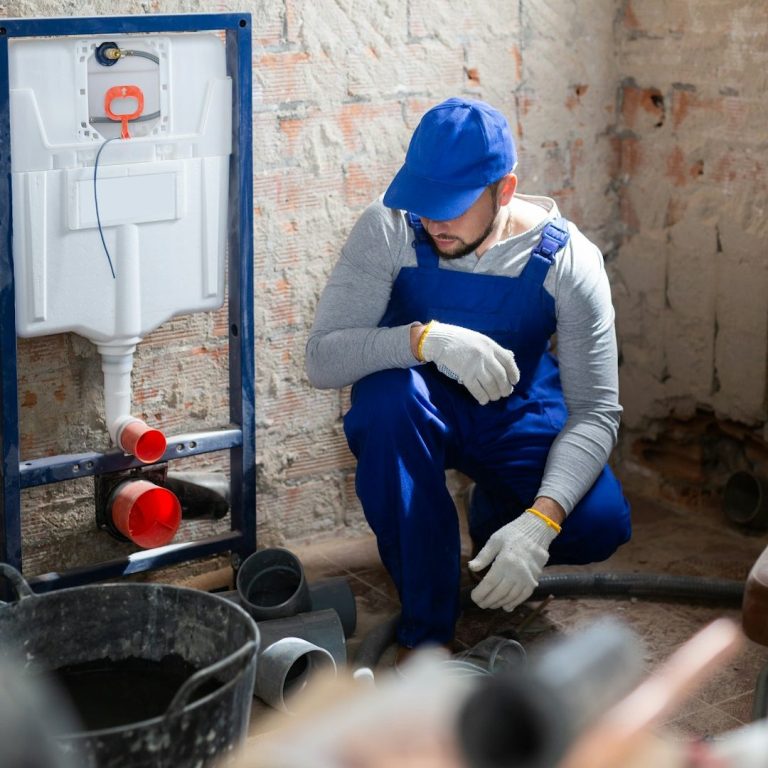 Handwerker in blauer Arbeitskleidung bei Sanitärinstallationsarbeiten.