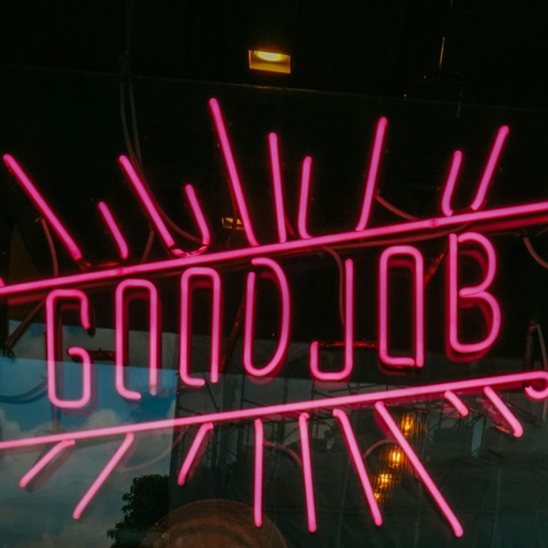 Neonlicht-Schriftzug "GOOD JOB" in pink mit strahlenden Linien.